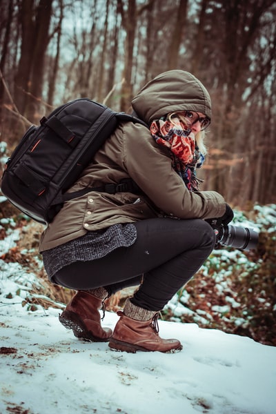 女人布朗风雪衣拿着相机蹲在冰雪覆盖的地面白天

